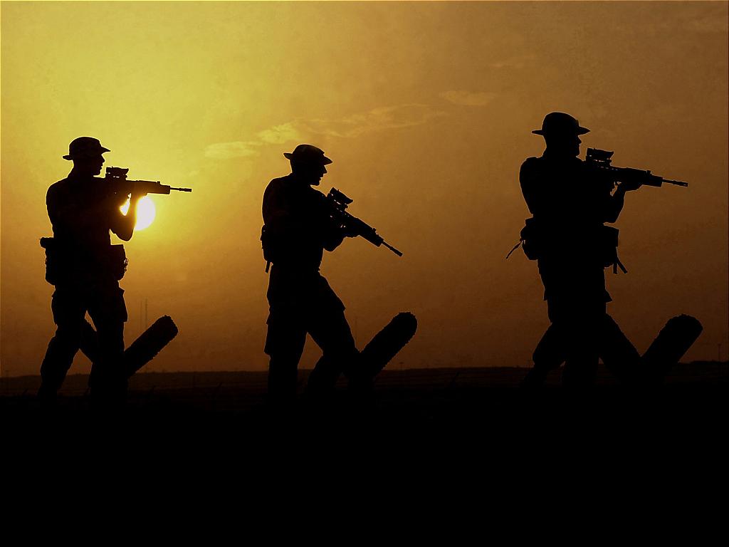 Three people with guns walking in as the sun is setting