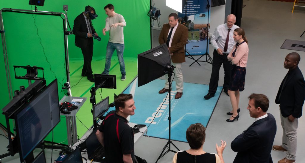 A group of people stood around a green screen trying on the VR headset.