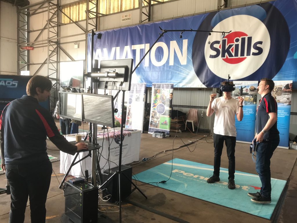 An exhibition set-up with a large banner on the wall that says "Aviation Skills" and three people in a VR headset