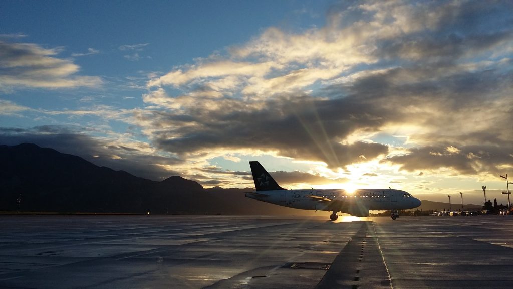 An airport runway. The sky is blue with the sun setting over an aeroplane