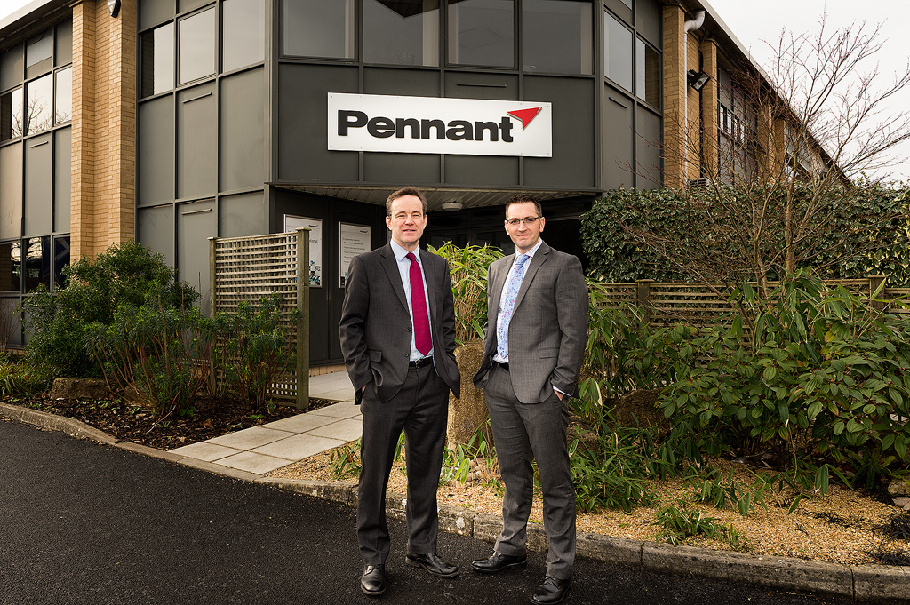 Two individuals standing in front of a building with a sign that reads “Pennant.”