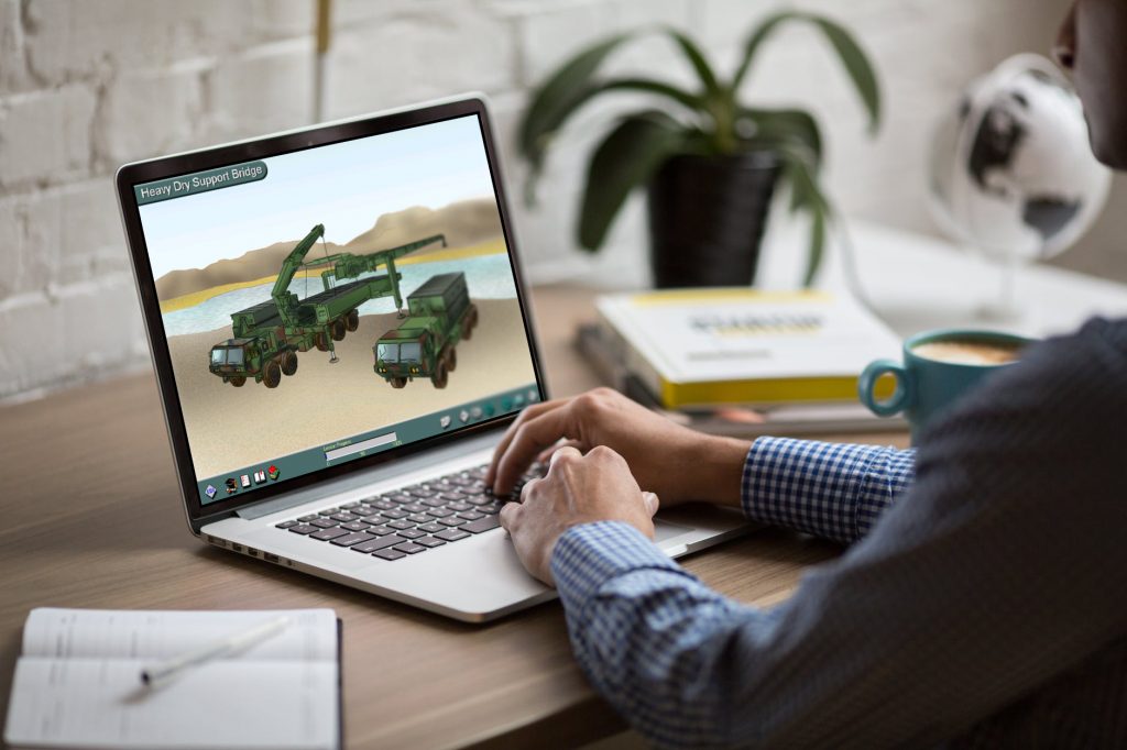 A mocked up computer screen with computer based learning on the screen. The learning includes a visual of army vehicles. The laptop is being operated by a person wearing a smart shirt.