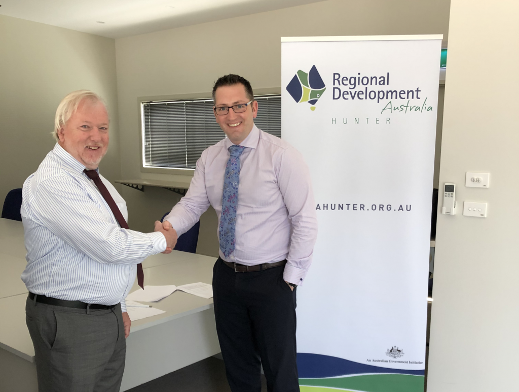 Two people shaking hands in from of a pop-up banner that says "Regional Development Australia" on it.