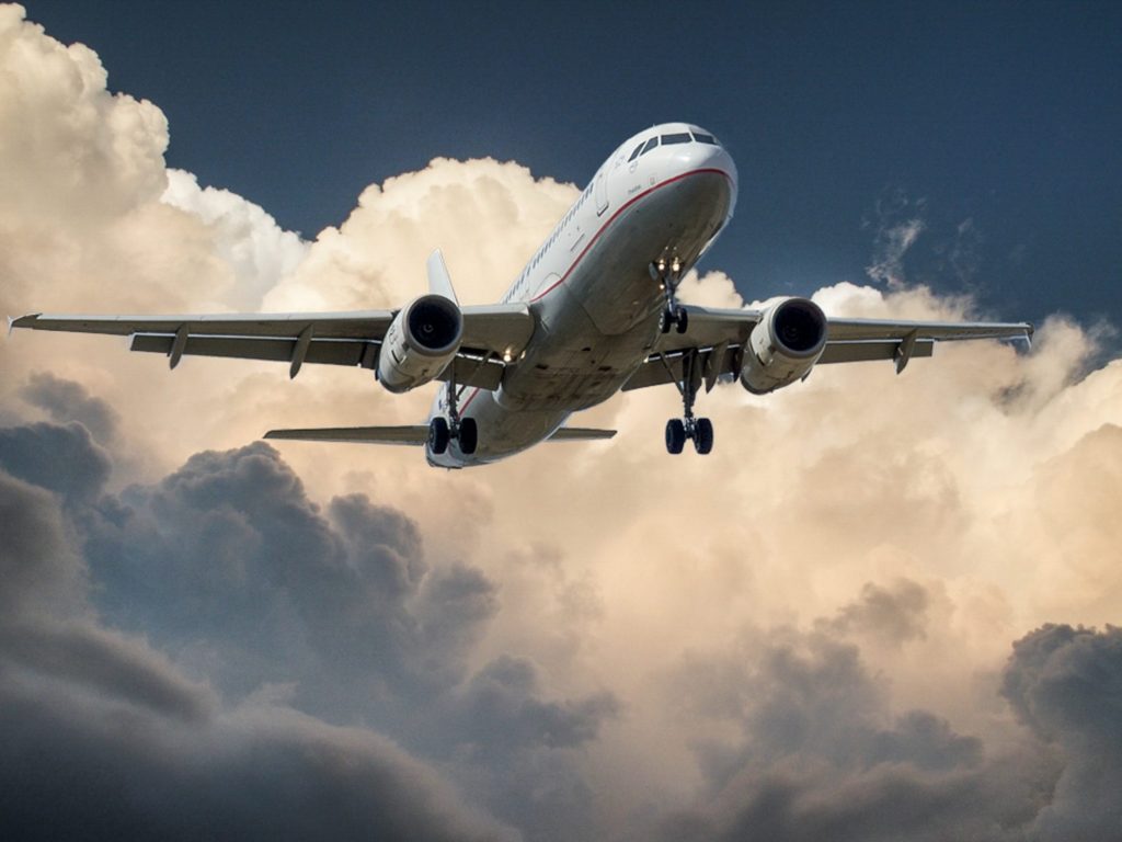 An aeroplane in the sky. There are lots of white clouds and a red line on the plane