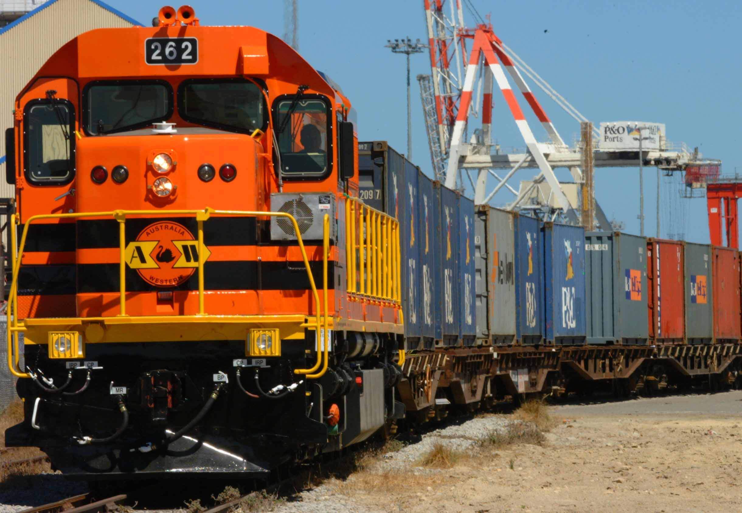 A cargo train with a variety of coloured containers. The front of the train is orange and looks like it's slowly moving on the tracks.